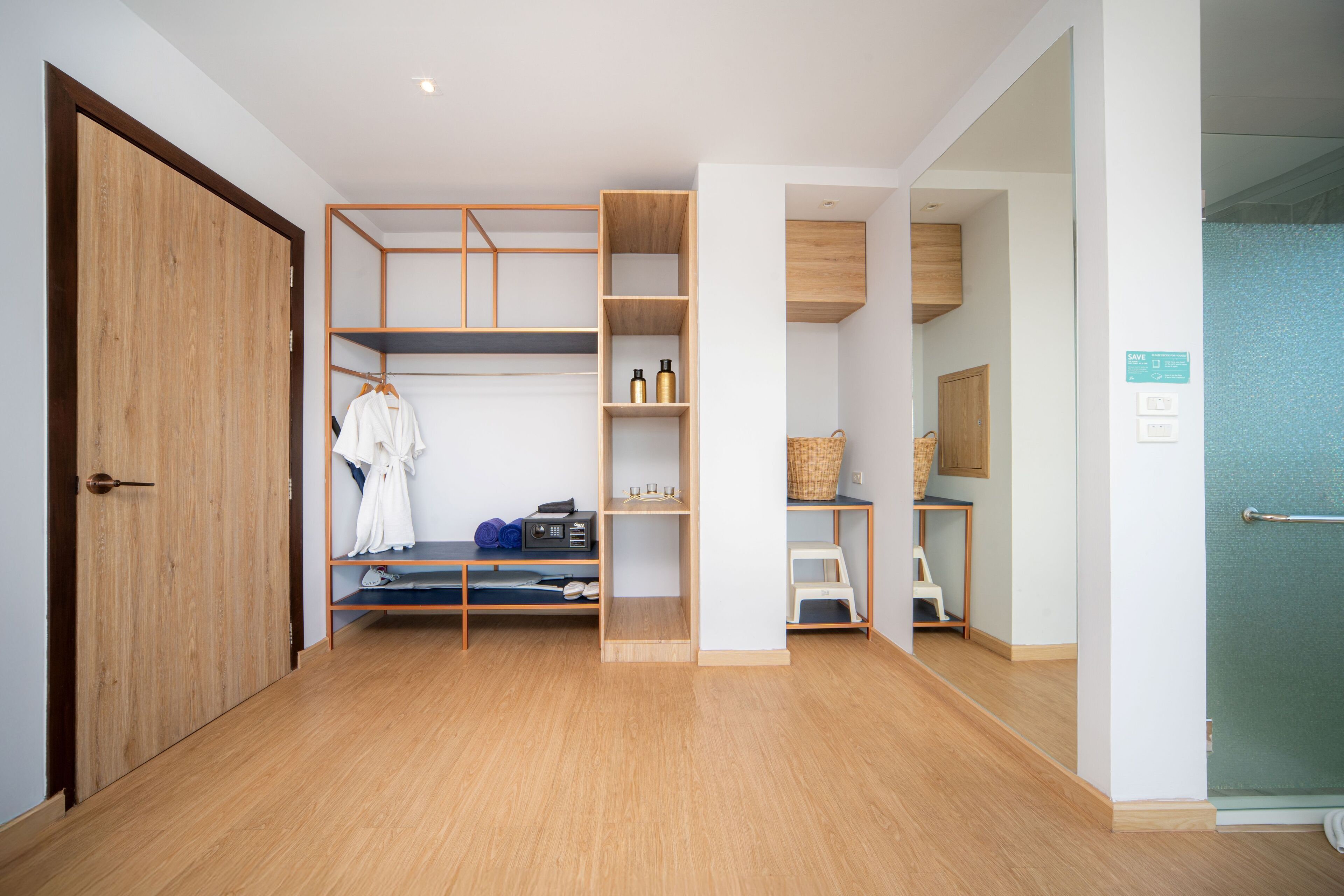 Une chambre moderne avec une armoire en bois, des étagères contenant divers objets, un petit coin salon et une douche en verre.