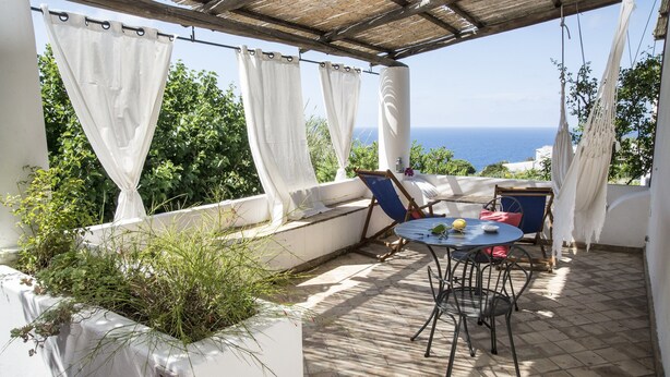Un área de estar al aire libre techada con una mesa y sillas, con vistas a un paisaje marino.