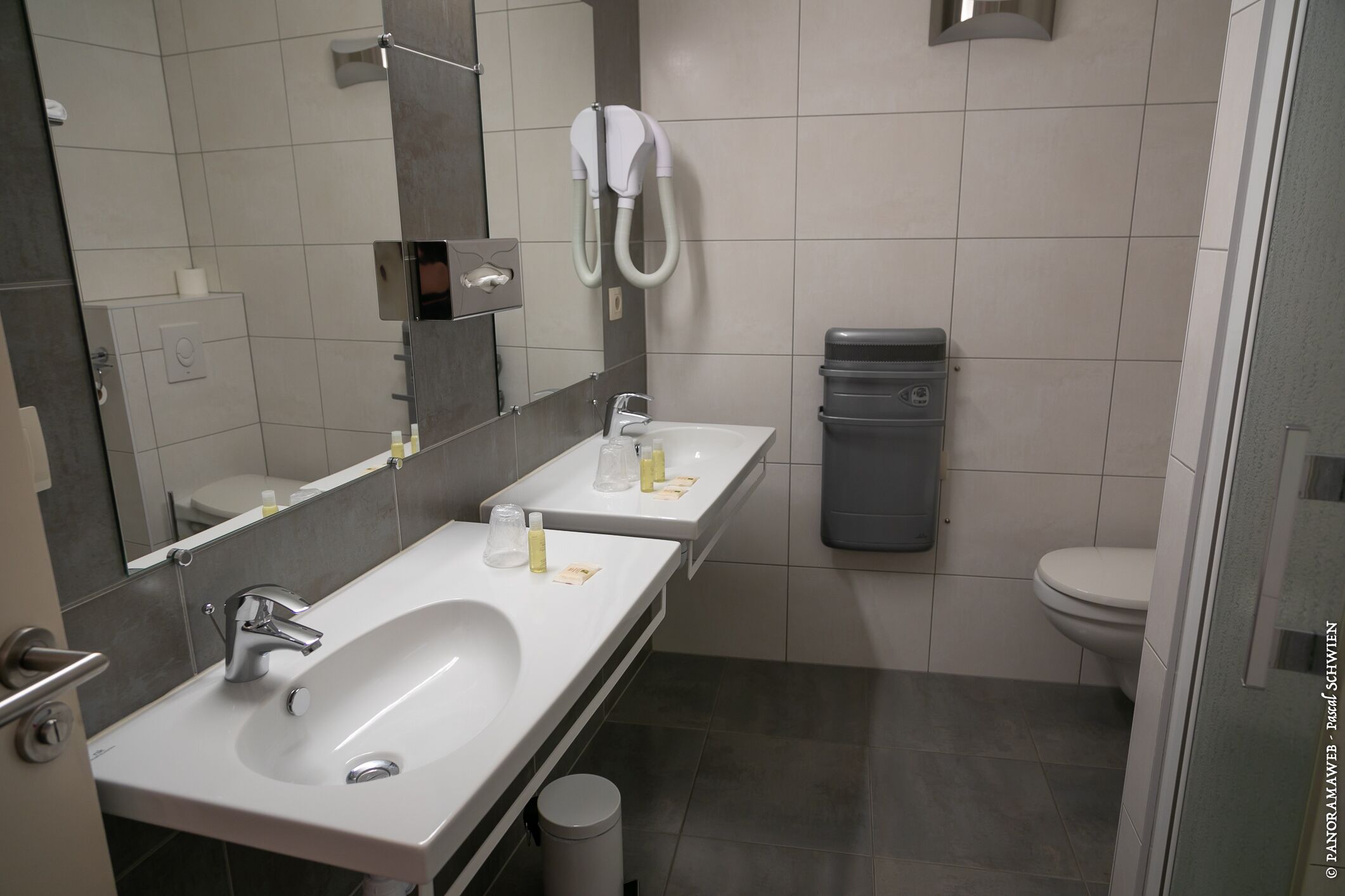 A modern bathroom with two sinks, a toilet, and a shower.