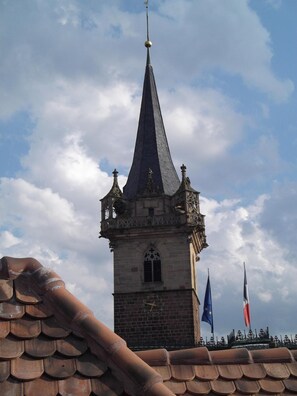 A tower with a pointed roof and a clock face, surrounded by flags. - Hôtel La Cloche (Obernai)