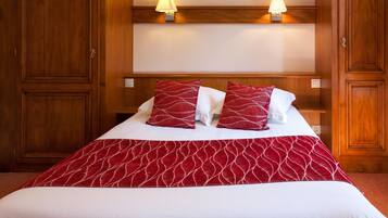 A hotel room with a large bed, two bedside lamps, wooden paneling, and a red and white patterned bedspread.