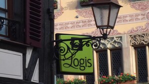 En byggnad med en grön skylt där det står ”Logis” och dekorativa fönsterlådor med blommor.