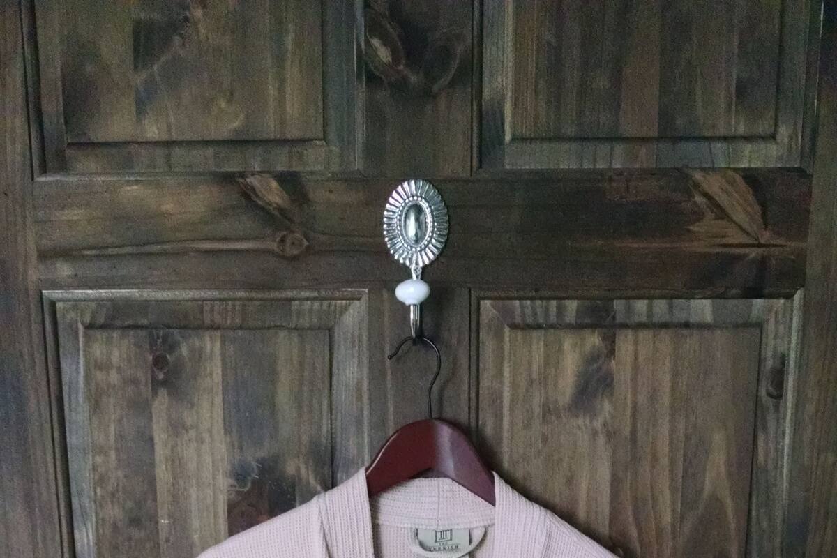 A beige robe hanging on a wooden door with a metal hook.