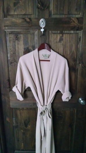 Une robe beige est suspendue à un crochet métallique sur une porte en bois.