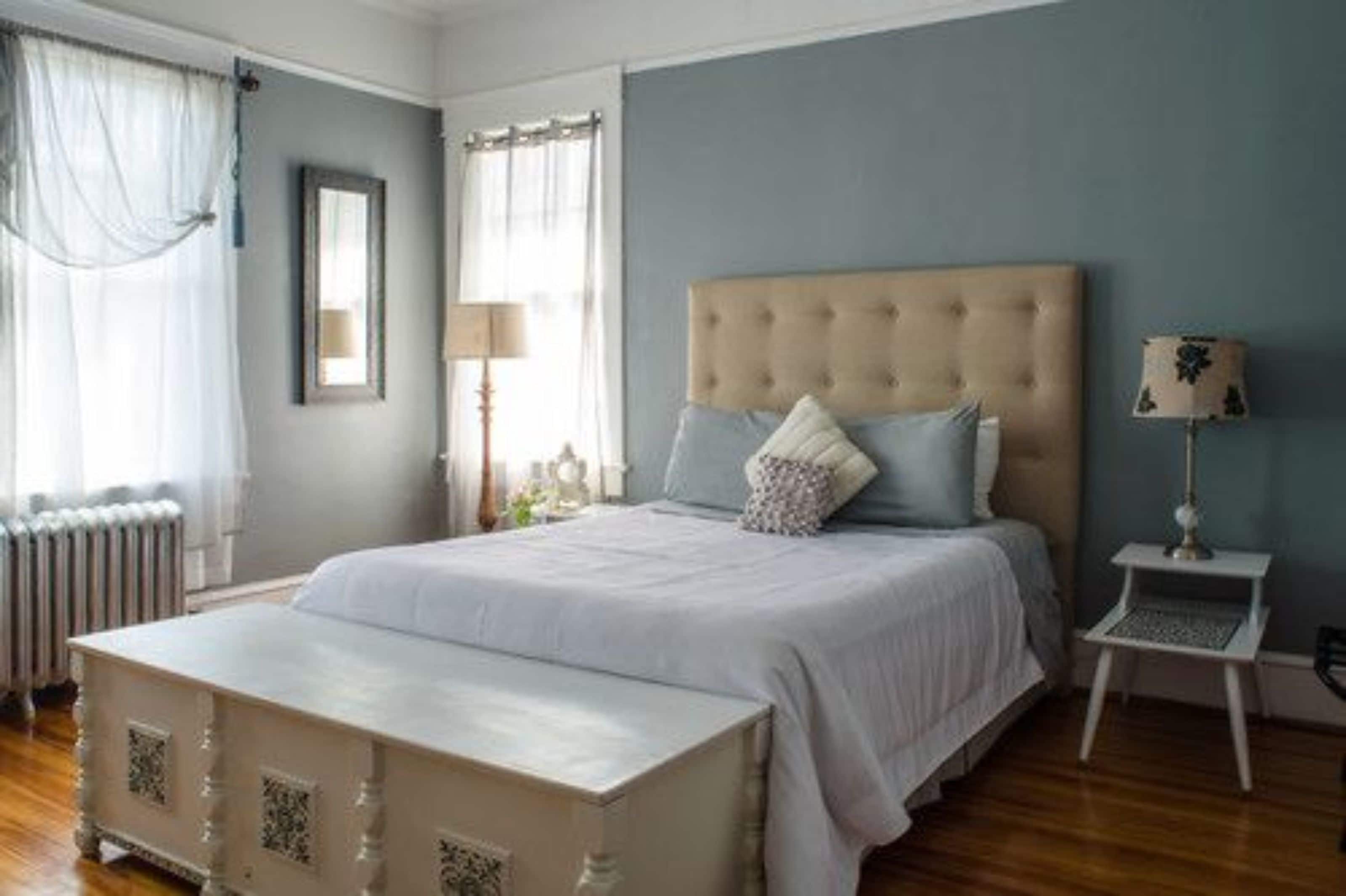 A bedroom with a large bed, a bedside table, a lamp, and a window with curtains.