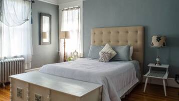 A bedroom with a large bed, a bedside table, a lamp, and a window with curtains.