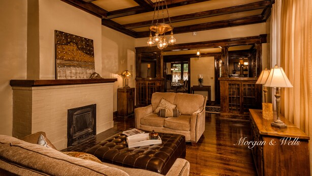 A cozy living room with a fireplace, a sofa, a leather ottoman, and a chandelier. - Morgan and Wells B&B (Shelby)