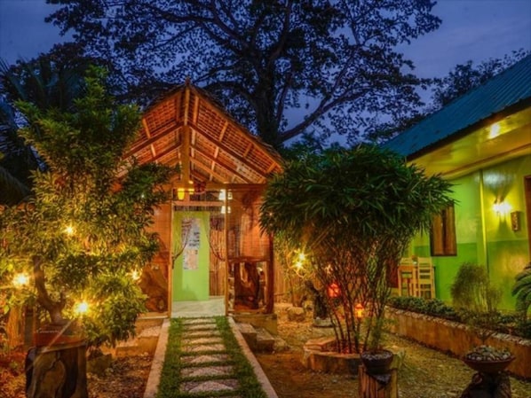 A traditional wooden structure with a thatched roof, surrounded by lush greenery and a well-maintained garden path.