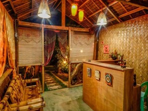 A wooden reception desk with a woven wall backdrop, a bamboo bench, and a staircase leading to a garden area.