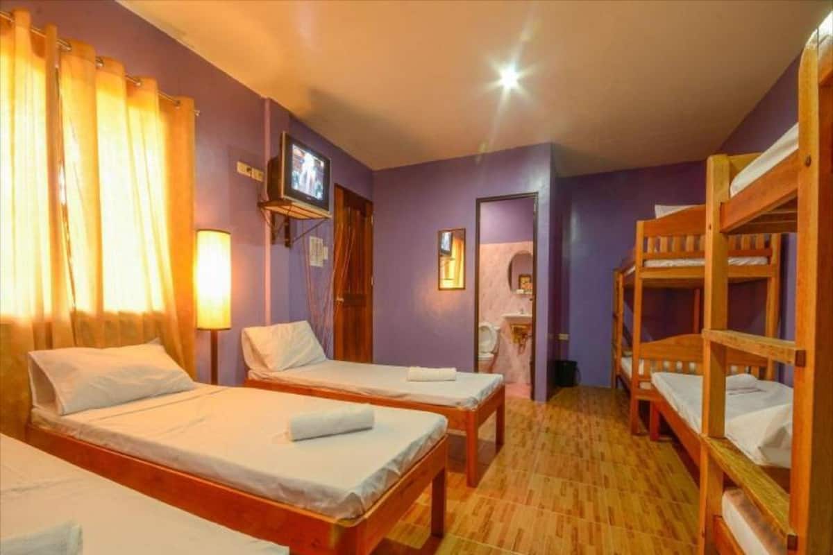 Ein Zimmer mit zwei Einzelbetten, einem Fernseher, Holzbettkästen und einer Badezimmertür.