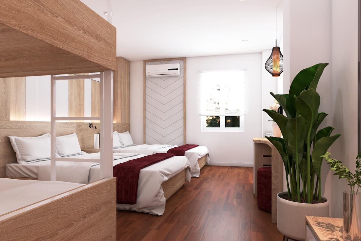 Een moderne hotelkamer met een stapelbed, een bureau met stoel, een grote potplant en een raam met jaloezieën.