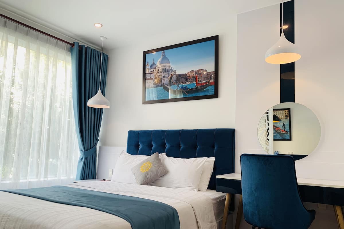 Hotelkamer met een bed, een bureau, een stoel, een groot raam met gordijnen en een stadsgezicht op een schilderij.
