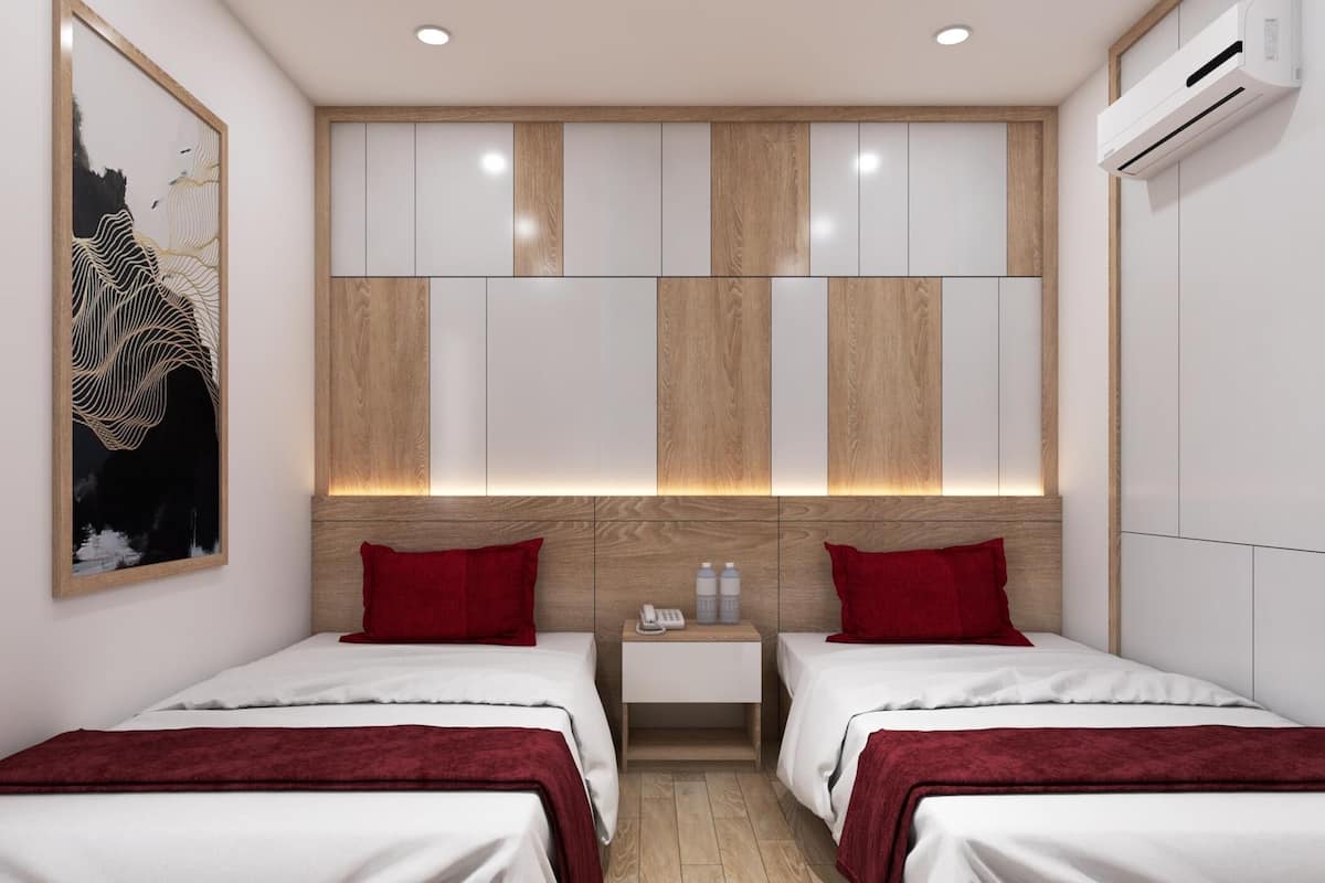 Hotelkamer met twee bedden, een houten hoofdbord, een wandairconditioner en een nachtkastje met telefoon en waterflessen.