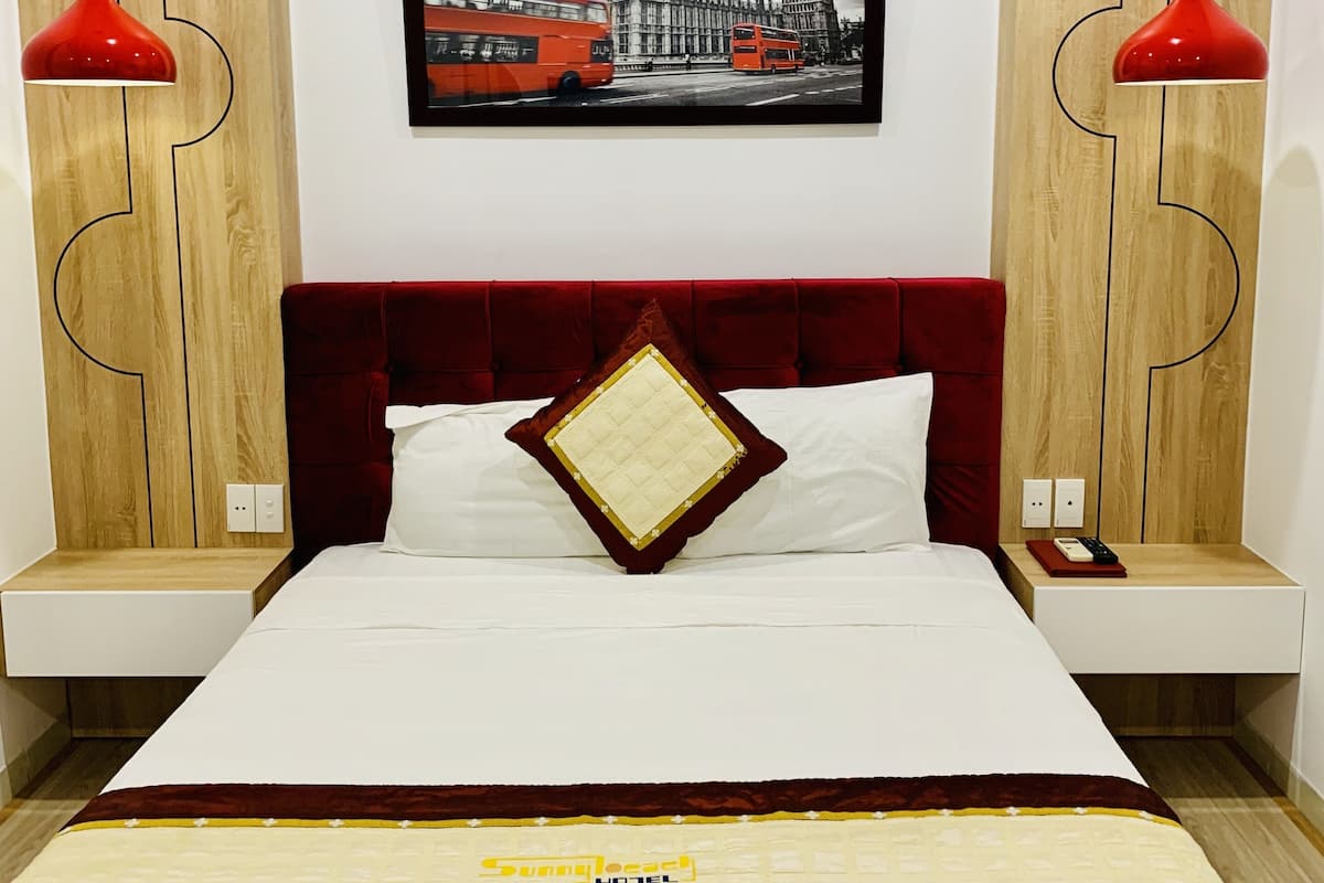 Hotelkamer met een groot bed, een rode hoofdbord, een ingelijst stadsbeeld en twee rode hanglampen.