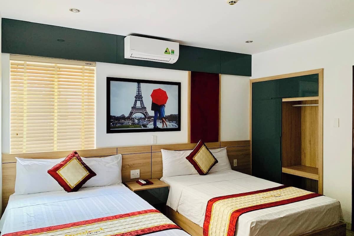 Een hotelkamer met twee bedden, een groot beeld van de Eiffeltoren, een airconditioning en een raam met jaloezieën.