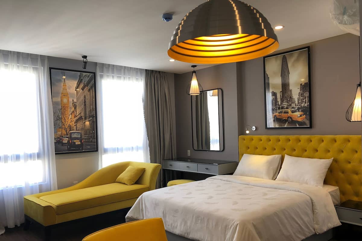 Een hotelkamer met een bed, een gele fauteuil, een bureau en een groot raam met uitzicht op een bekende toren.
