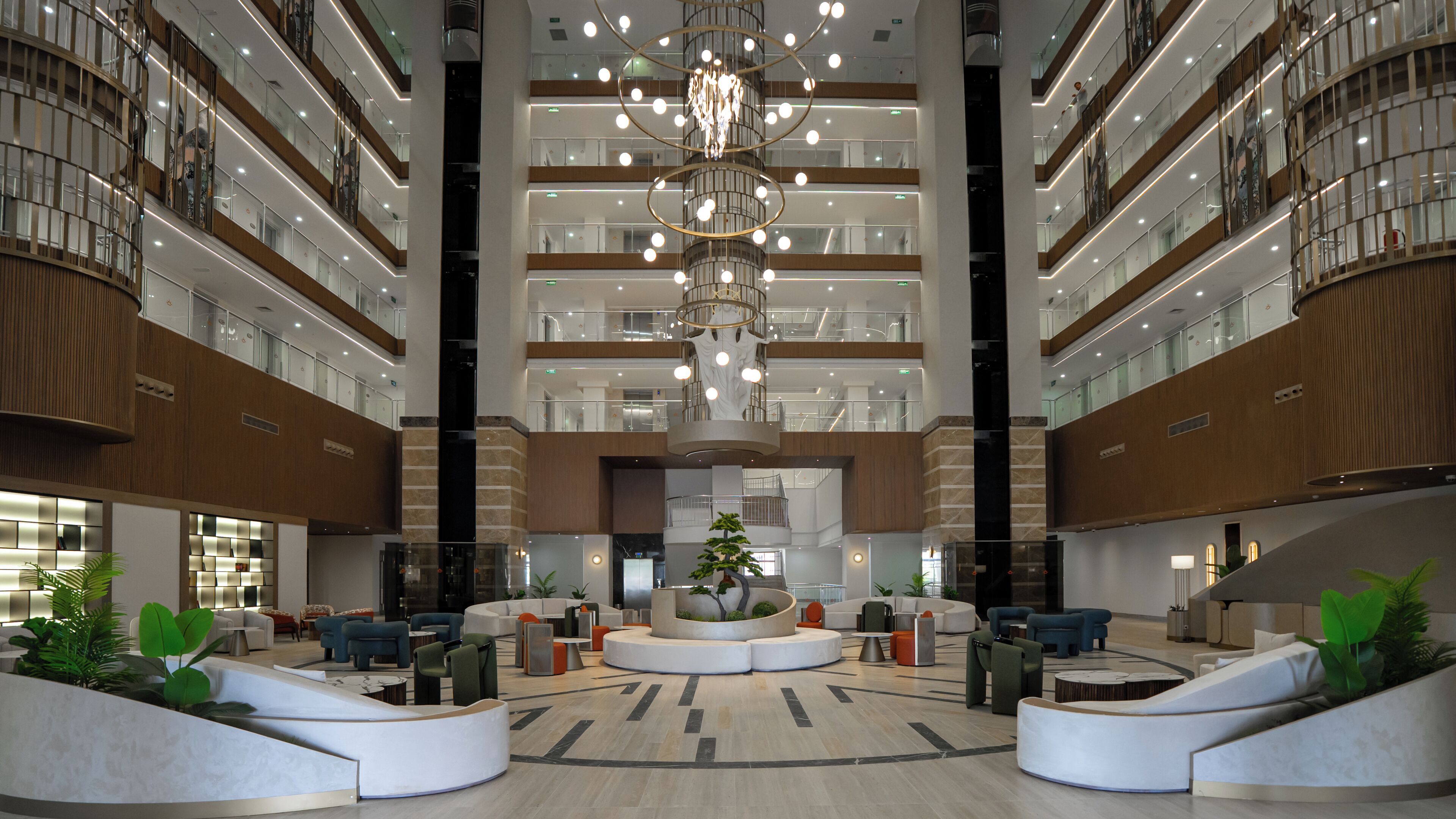A spacious lobby with a central chandelier, multiple seating areas, and a large plant centerpiece.