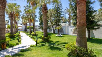 Un sendero que atraviesa una zona ajardinada con palmeras y un edificio blanco con arcos.