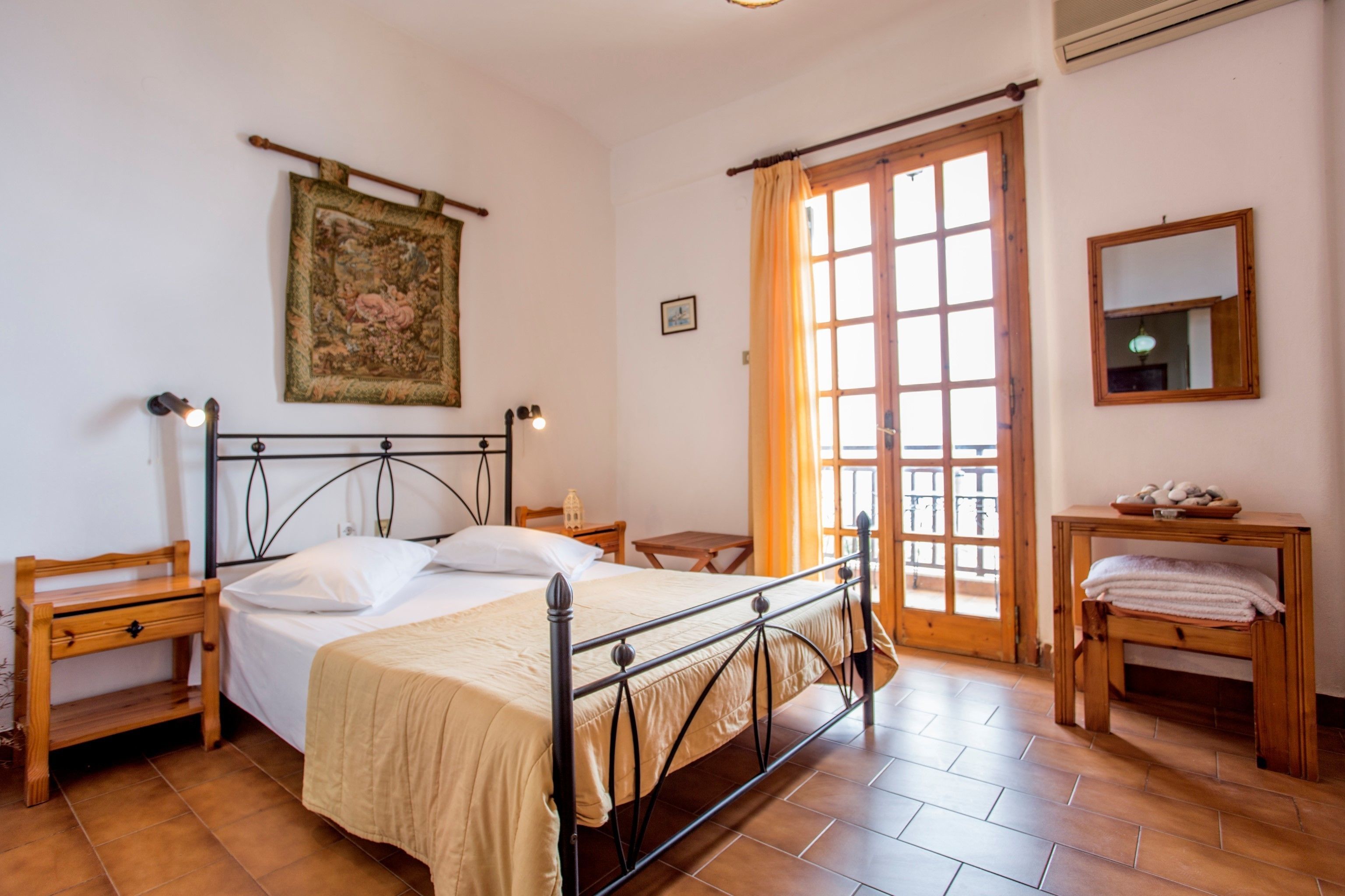 A bedroom with a bed, bedside tables, a wooden bench, a window with curtains, and a wall-mounted mirror.