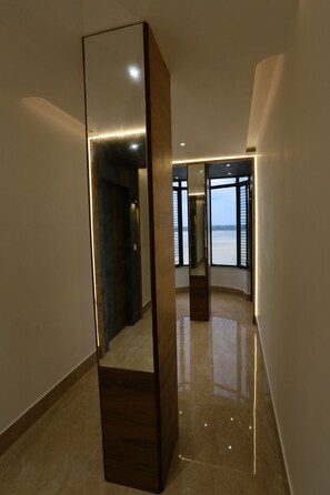 A hallway with a large mirror, a polished floor, and a view of a body of water through a window. - A Palace on River - Rashmi guest House (Varanasi)