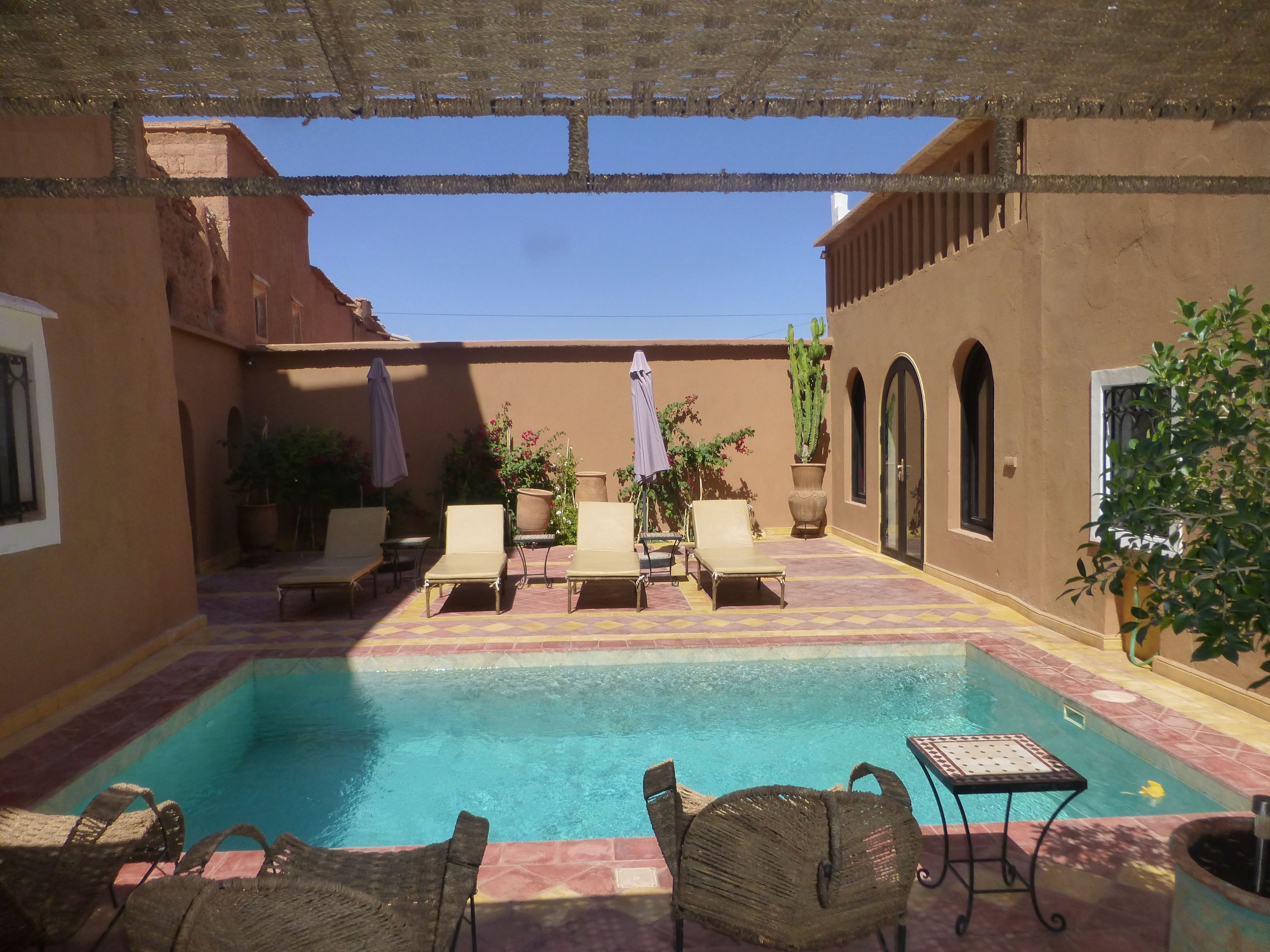 A pool area with lounge chairs and umbrellas, surrounded by walls and potted plants.