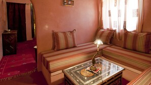 A cozy room with a high wooden ceiling, a sofa set, a small table with a lamp, and a decorative wall hanging. - Kasbah La Cigogne (Aït Benhaddou)
