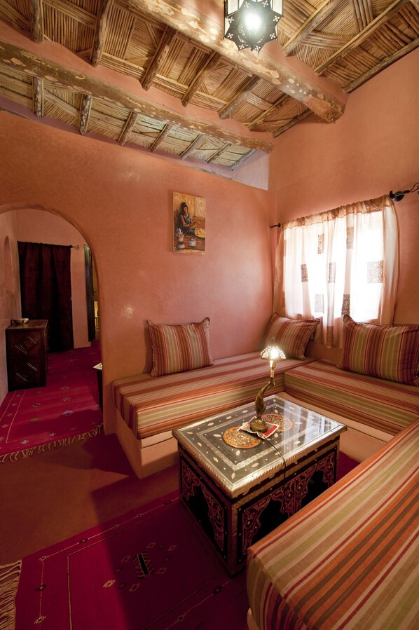 Una habitación acogedora con un alto techo de madera, un conjunto de sofá, una pequeña mesa con lámpara y un adorno colgante en la pared.