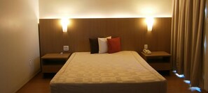 A hotel room with a large bed, two bedside tables, a nightstand, and a wall-mounted lamp. - Sete Lagoas Residence Hotel (Sete Lagoas)