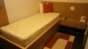A small, single-bed room with a wooden headboard, a bedside table with a phone, and a checkered rug on the floor.