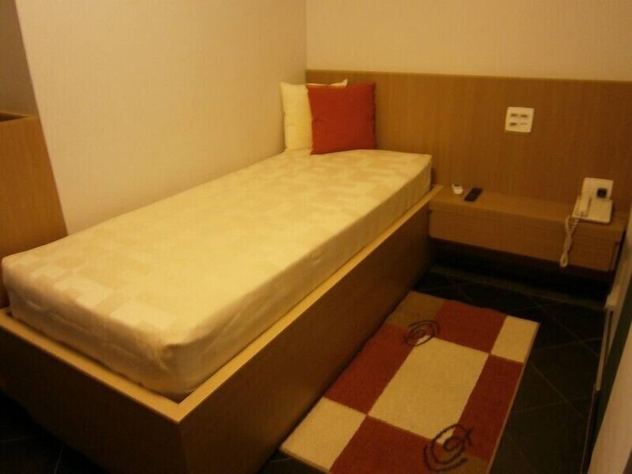A small, single-bed room with a wooden headboard, a bedside table with a phone, and a checkered rug on the floor.
