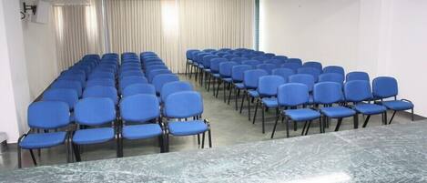 A conference room with rows of blue chairs and a marble table.