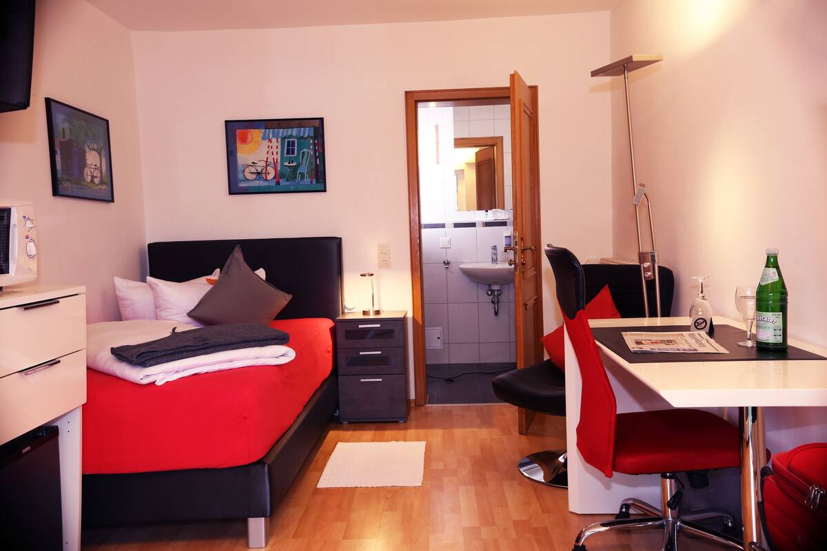 Ein Hotelzimmer mit Bett, Schreibtisch, Stuhl, Spiegel und einem durch eine offene Tür einsehbaren Badezimmer.