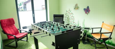 A room with a foosball table, two chairs, a table, and a window.