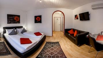 A modern hotel room with a large bed, a sofa, a dining area, and a TV.