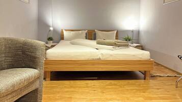 A bedroom with a wooden bed, a chair, a bedside table with a lamp, and a small plant.