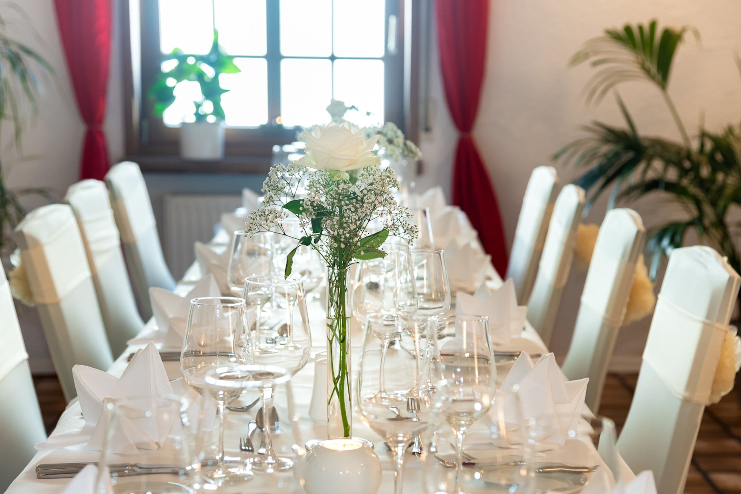 Une table à manger dressée pour un événement formel, avec des nappes blanches, de la verrerie et un centre de table composé de fleurs blanches.