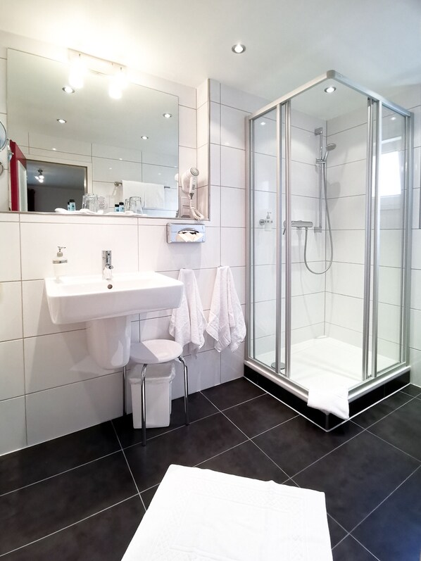 A modern bathroom with a glass-enclosed shower, a white sink, and a large mirror.