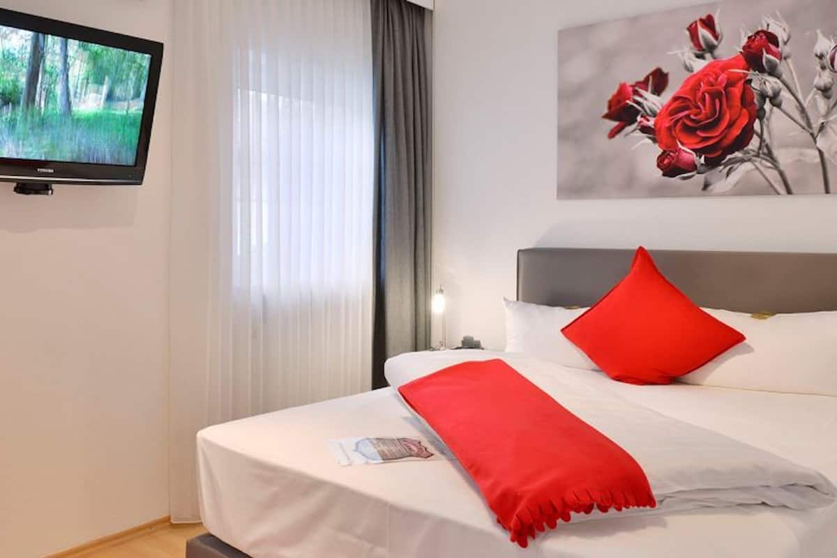 Ein Hotelzimmer mit Bett, einem an der Wand befestigten Fernseher und einem Rosenbild.