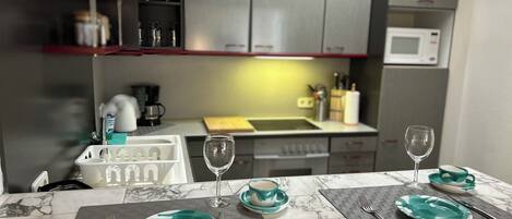 A kitchen with a marble countertop, a sink, and cabinets. There are wine glasses and plates on the counter.