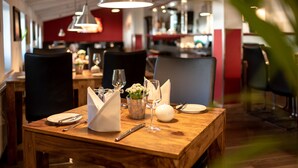 Une table à manger dressée avec une assiette blanche, des couverts en argent, un verre à vin, une bougie et un petit vase avec des fleurs.