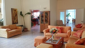 A spacious living room with a sofa set, a coffee table with a vase of flowers, and a bookshelf. - Ipsos Beach (Corfu)
