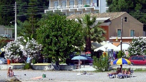 A hotel with a balcony, located near a beach with clear turquoise water. - Ipsos Beach (Corfu)