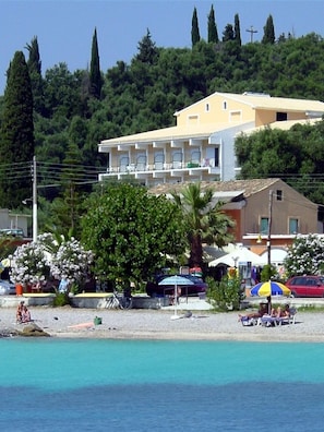 Ett hotell med balkong, beläget nära en strand med kristallklart, turkosfärgat vatten.