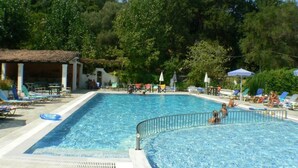 A swimming pool with lounge chairs and umbrellas, surrounded by trees. - Ipsos Beach (Corfu)