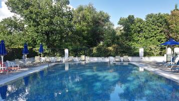 Una piscina rectangular con agua cristalina azul, rodeada de sillones de descanso y sombrillas azules.