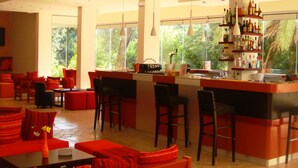 A spacious bar area with a high counter, multiple seating options, and a view of greenery outside. - Ipsos Beach (Corfu)