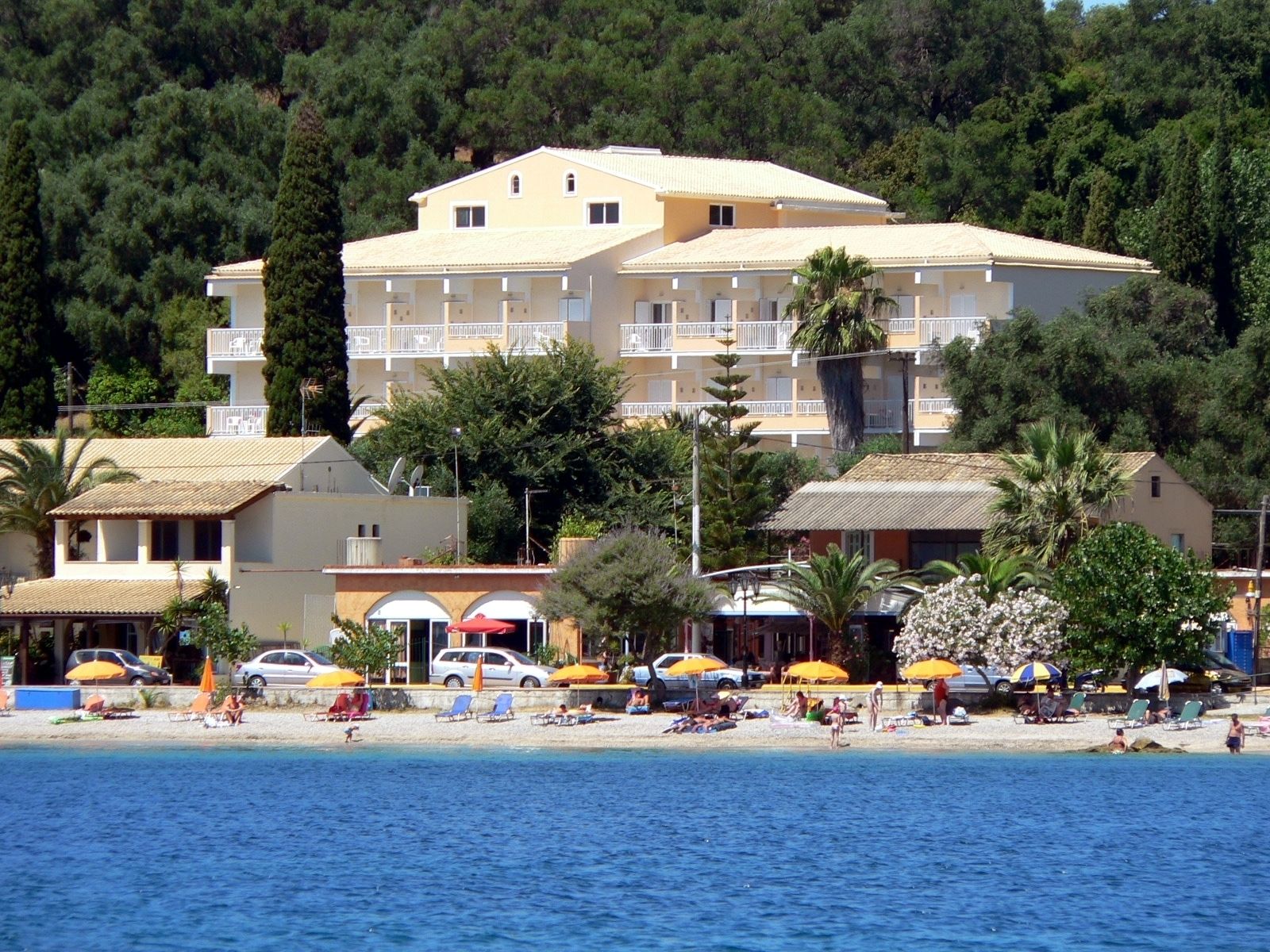 A coastal hotel with multiple floors, balconies, and a beach area with umbrellas and sun loungers.