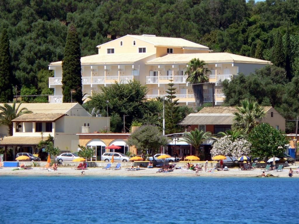 Un hôtel situé sur la côte, doté de nombreux balcons, avec une plage au premier plan et une colline boisée en arrière-plan.