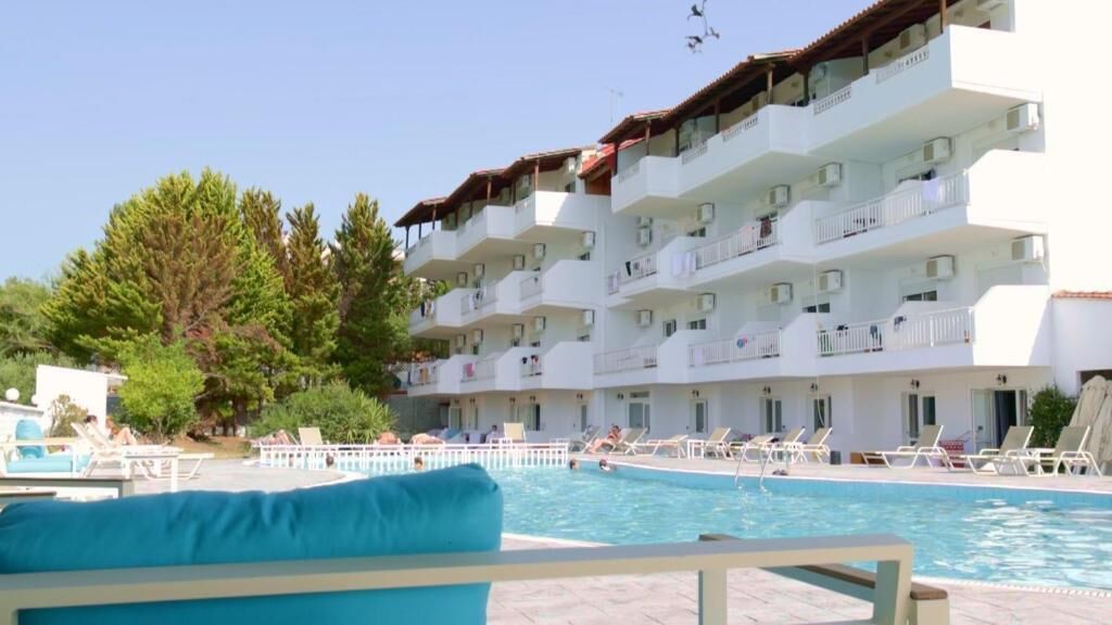 Hotel amb piscina, diversos balcons i cel blau.
