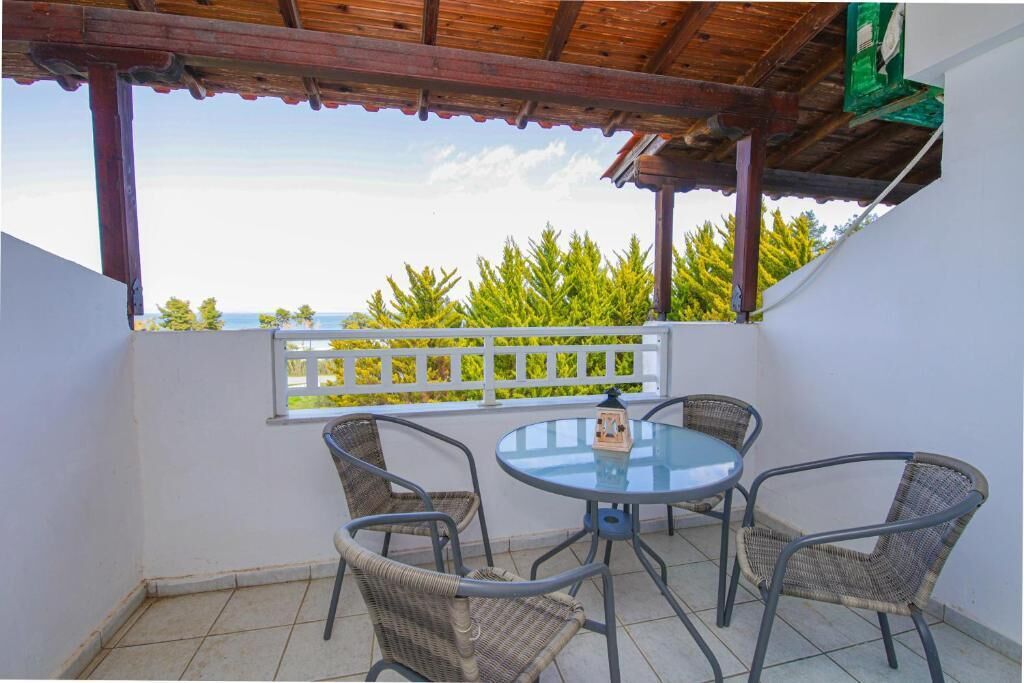 A covered outdoor seating area with a table and chairs, a view of greenery, and a white railing.